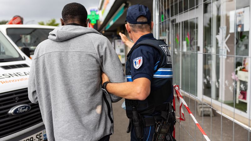 Stéphane guide un homme malvoyant qui tente de se frayer un chemin entre les voitures et les travaux en cours devant la pharmacie du centre commercial. © Jean-Félix Fayolle.